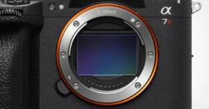 A close-up view of a camera lens mount with a visible sensor, featuring the text "E-mount" and "α 7R" on the camera body.