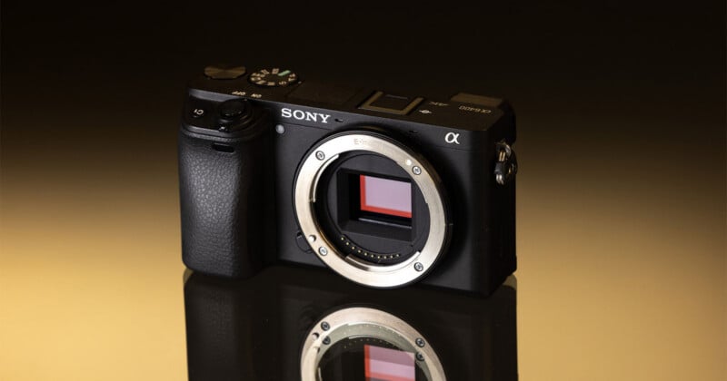 A black Sony Alpha 6400 mirrorless camera body sits on a reflective surface against a gradient brown background.