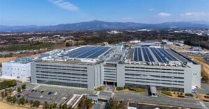 An aerial view of a large, multi-story Sony industrial facility with solar panels on the roof and a parking lot in the foreground.