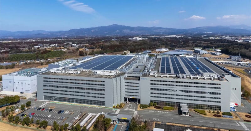 An aerial view of a large, multi-story Sony industrial facility with solar panels on the roof and a parking lot in the foreground.