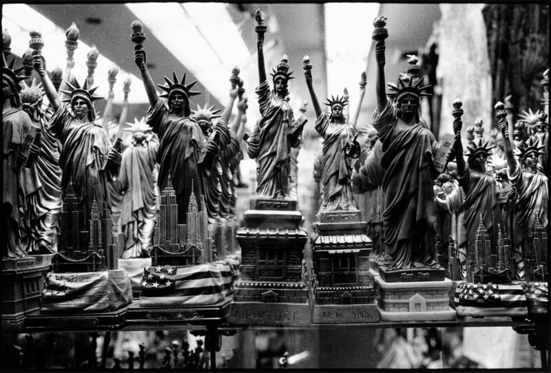 A collection of Statue of Liberty souvenir figurines arranged on a shelf, many featuring miniature New York City skylines.