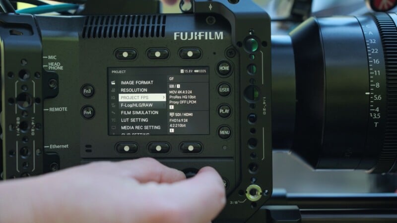 A hand adjusts the settings on a Fujifilm cinema camera screen displaying a project menu with resolution and frame rate options.