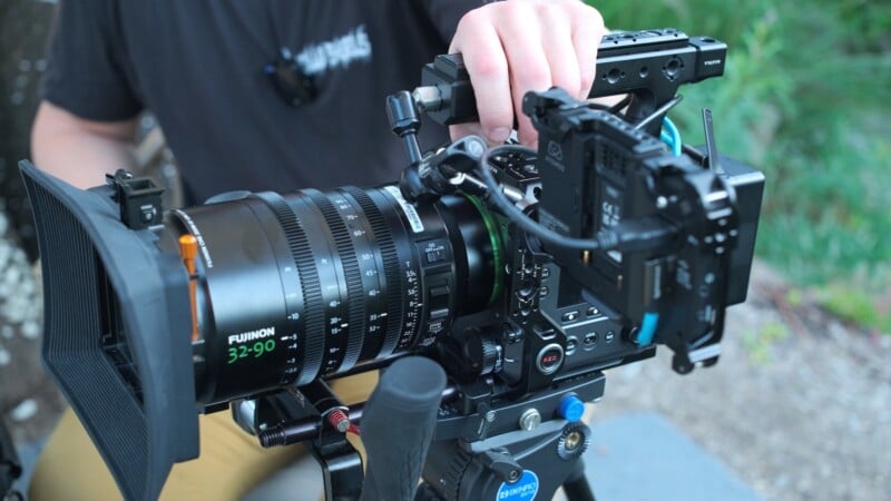 A person holds the top handle of a professional cinema camera rig equipped with a Fujinon 32-90 lens and an Atomos monitor.