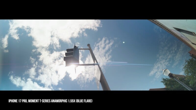 A low-angle shot looking up at a traffic light against a bright blue sky with scattered clouds, featuring a horizontal lens flare.