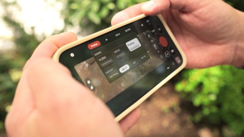 A person holds a smartphone displaying a video recording interface with codec and ProRes variant settings visible on the screen.