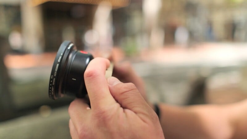 A person's hands hold a camera lens with a variable ND8-ND2000 filter attached, set against a blurred outdoor background.