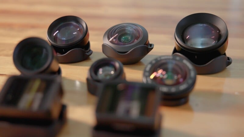 Several camera lenses and lens attachments are arranged on a wooden surface.