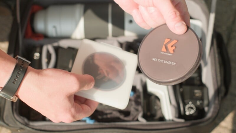 A person holds a K&F Concept camera lens filter in its case and a matching filter cap over an open camera bag.
