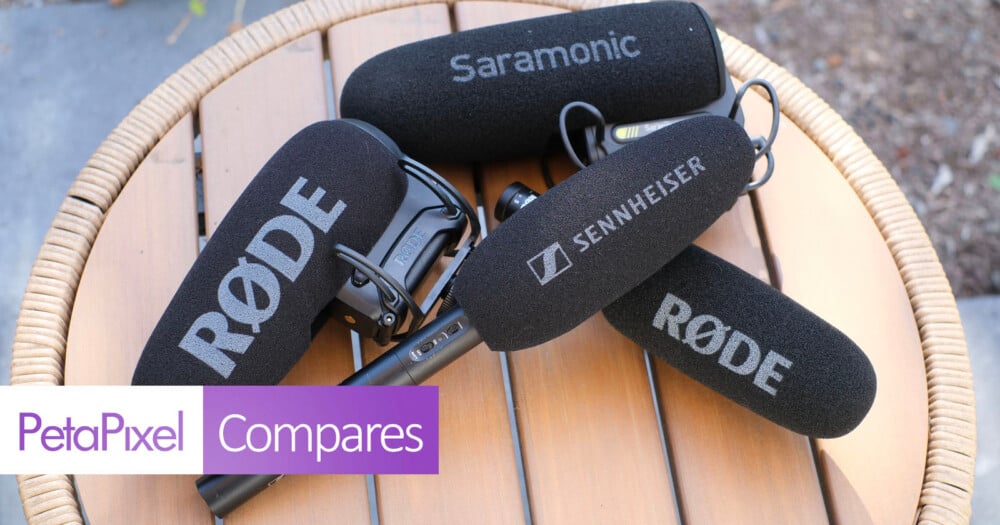 Four microphones with foam windscreens labeled Rode, Saramonic, and Sennheiser rest on a round wooden table.