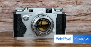 A silver Konishiroku camera with a Hexanon 48mm f/2 lens sits on a wooden surface against a wood-grain background, with a PetaPixel Reviews logo in the bottom right corner.