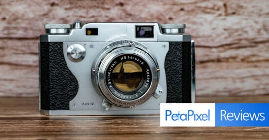 A silver Konishiroku camera with a Hexanon 48mm f/2 lens sits on a wooden surface against a wood-grain background, with a PetaPixel Reviews logo in the bottom right corner.