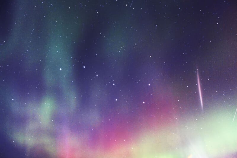 A vibrant aurora borealis displays green and magenta light across a dark, star-filled night sky.