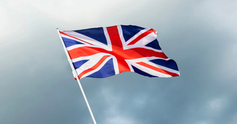 The Union Jack flag of the United Kingdom waves against a cloudy, grey sky.