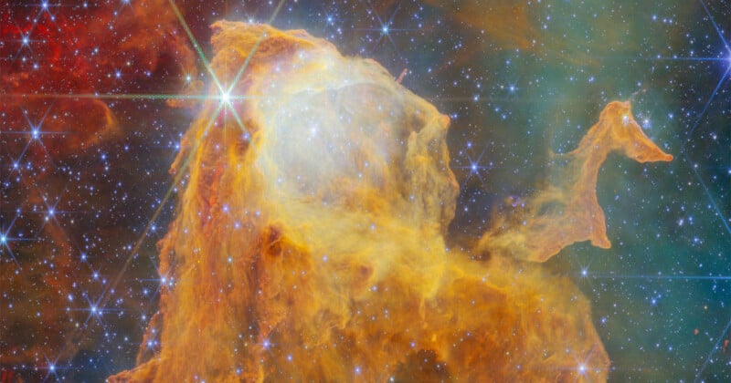 A vibrant nebula of orange and yellow gas clouds illuminated by bright, star-like points of light with distinct diffraction spikes.