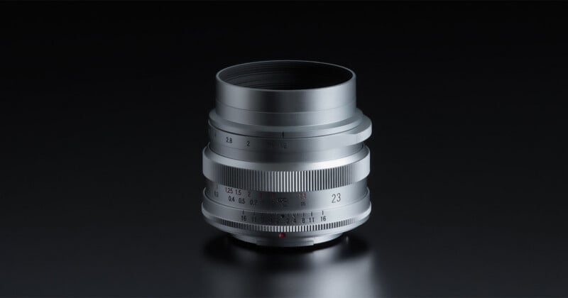 A silver camera lens with manual focus and aperture rings sits against a dark background.