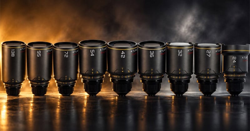 A row of nine black Atlas Orion cinema lenses arranged by focal length from 138mm to 24mm on a dark, reflective surface.