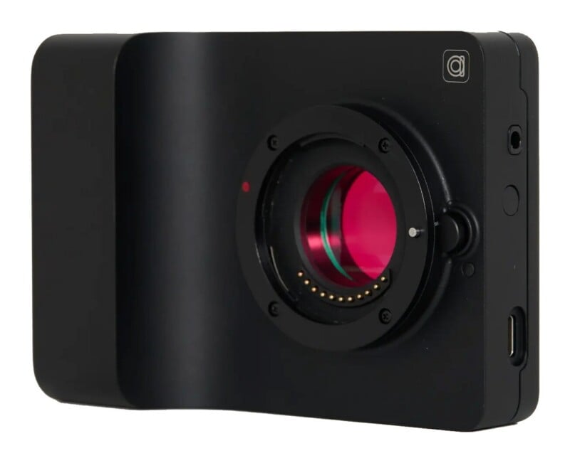 A black, minimalist digital camera body with a lens mount, a red-tinted sensor, and a USB-C port on the side.