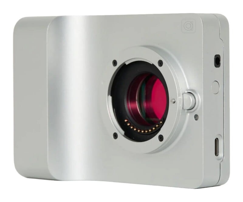 A silver, rectangular digital camera body with a central lens mount, a red-tinted sensor, and a USB-C port on the side.