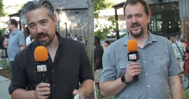 Two men stand outdoors holding microphones with orange foam covers, each featuring a small camera logo on the base.