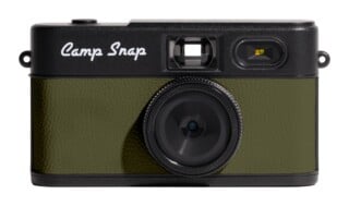 A front-facing digital camera with a black body, olive green textured grip, and the text "Camp Snap" in white script.