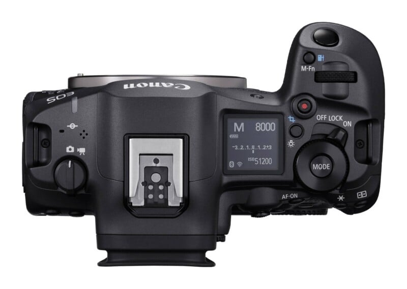 Top-down view of a black digital camera body showing the LCD display, shutter button, mode dial, and hot shoe mount.