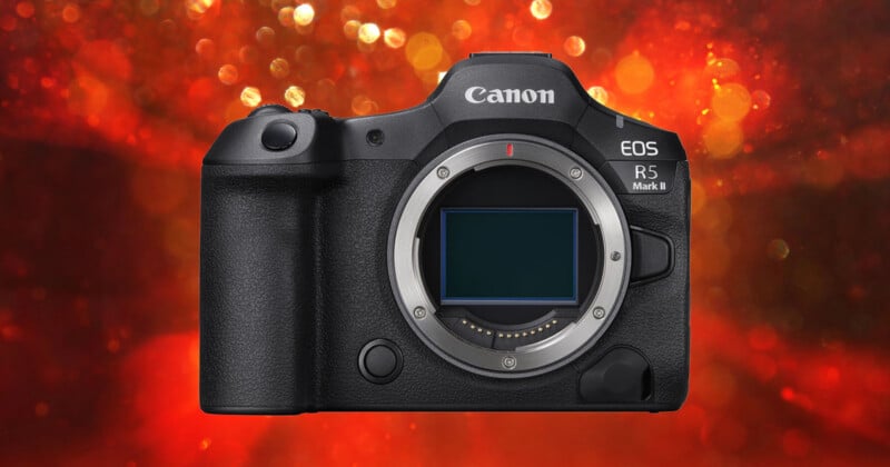 A front view of a black Canon EOS R5 Mark II mirrorless camera body against a blurred red bokeh background.