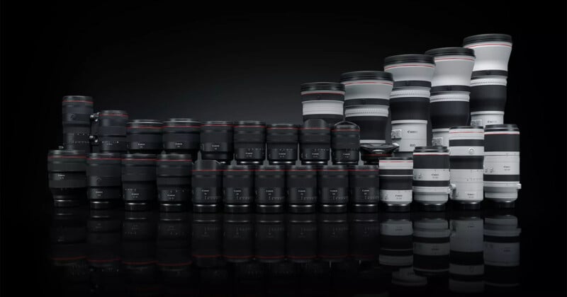 A collection of various Canon camera lenses arranged in rows on a reflective black surface against a dark background.