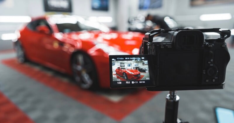 A camera on a tripod records a red sports car parked in a garage, with the car's image displayed on the camera's screen.
