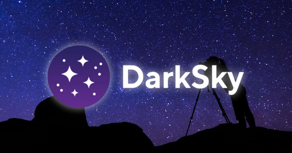 A silhouette of a person using a camera on a tripod stands on a rocky hill against a starry night sky, with a DarkSky logo.