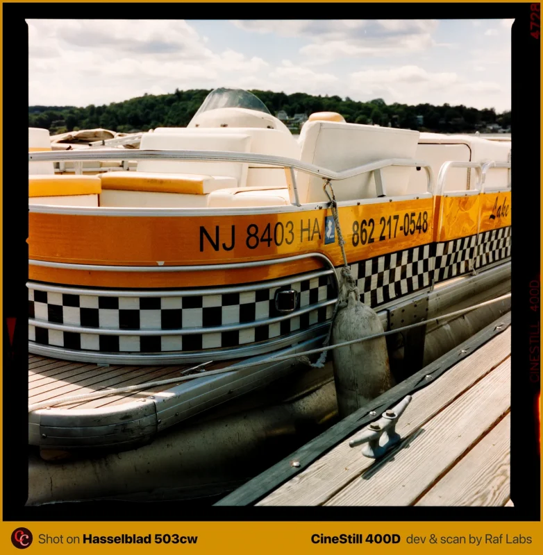 A yellow and white pontoon boat with a checkered pattern along its side is docked at a wooden pier.