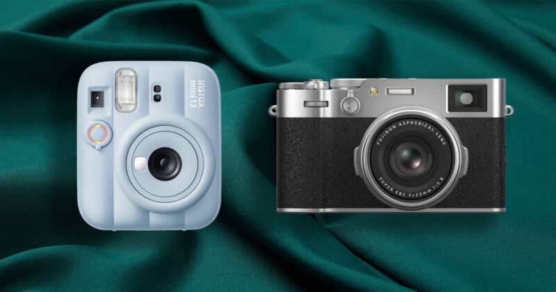 A light blue Instax mini 13 instant camera and a silver and black Fujifilm X100V digital camera sit side-by-side on a dark green fabric background.
