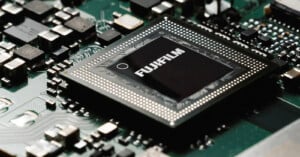 A close-up view of a black square computer chip labeled "FUJIFILM" mounted on a green circuit board with various electronic components.