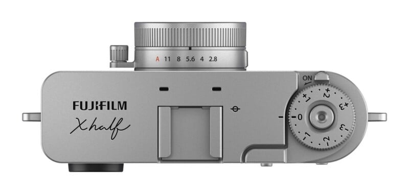 Top-down view of a silver Fujifilm X-half camera, showing the aperture ring, hot shoe, and exposure compensation dial.