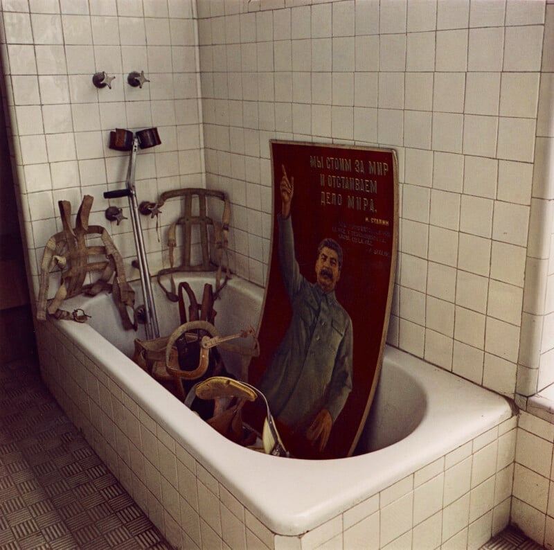 A bathtub filled with orthopedic harnesses, crutches, and a poster of Joseph Stalin pointing upward.