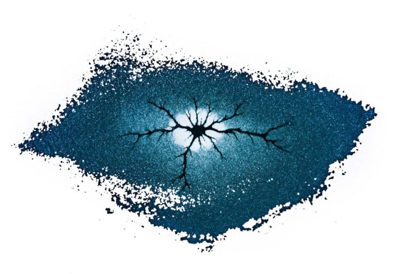 A dark blue, textured, rectangular shape with frayed edges features a central black starburst pattern that radiates outward.