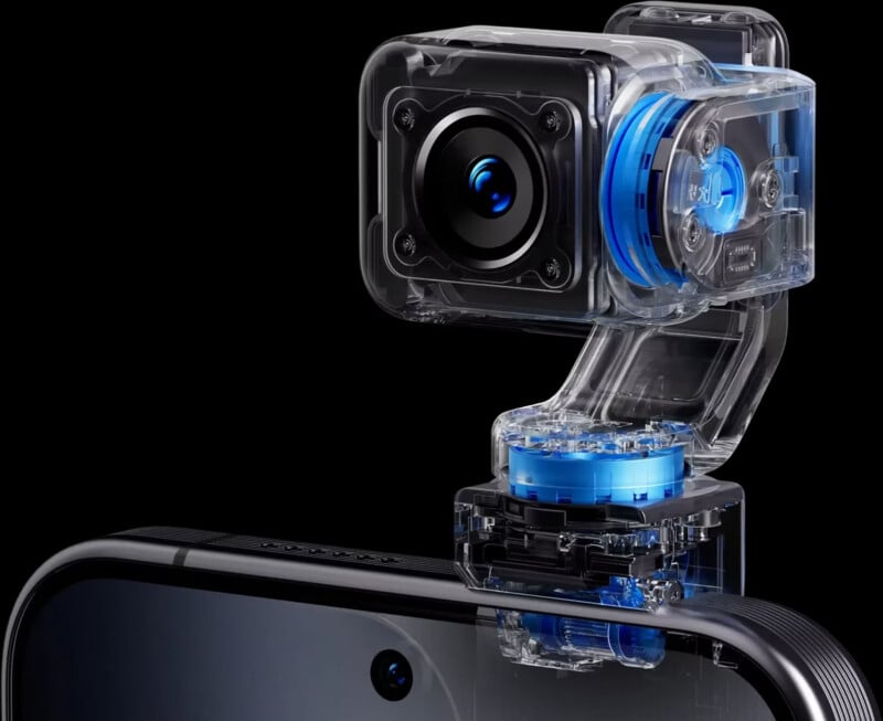 A transparent, mechanical gimbal camera attachment is mounted onto the top edge of a smartphone.