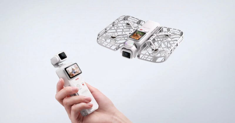 A hand holds a white handheld gimbal camera with a screen, while a matching white drone with a protective cage flies in the air nearby.