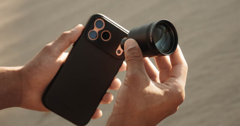 A person holds a black smartphone with a large, detachable telephoto lens being attached to the camera array.