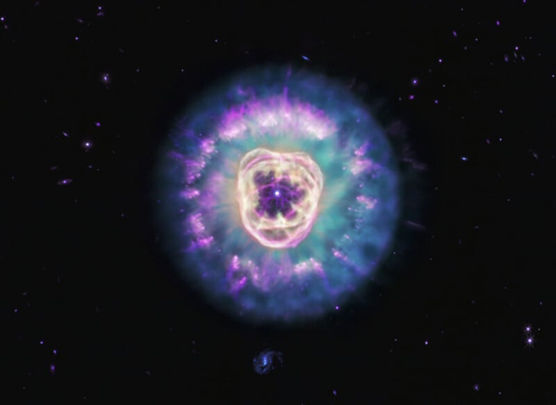 A vibrant, glowing planetary nebula with concentric rings of purple, blue, and gold gas surrounding a bright central star.