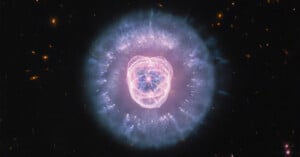 The Eskimo Nebula glows in space with a bright, pink-tinted inner core surrounded by a large, translucent blue shell of gas.