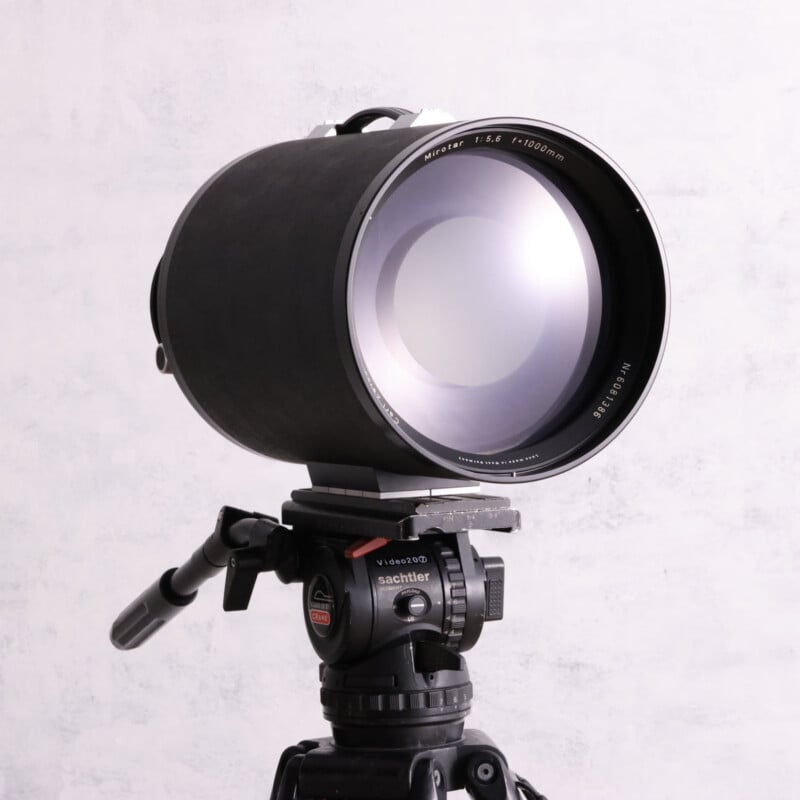 A large Carl Zeiss Mirotar 1000mm f/5.6 telephoto lens mounted on a Sachtler Video 20 tripod head against a light gray background.