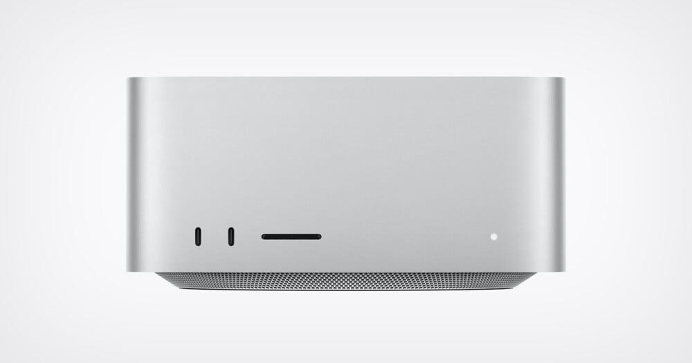 A front-facing view of a silver, rectangular desktop computer with two USB-C ports, an SD card slot, and a small status light on the front panel, sitting above a perforated base.