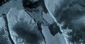 An aerial view of a frozen landscape featuring jagged ice formations, dark water channels, and expansive, textured ice sheets.