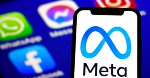 A smartphone screen displays the blue Meta logo and company name, with blurred app icons for Facebook, WhatsApp, and Messenger in the background.