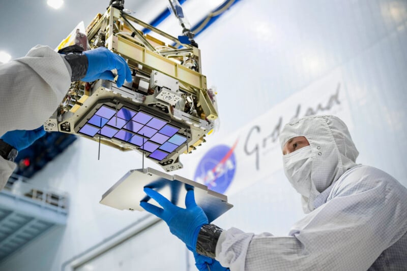 A technician in a cleanroom suit and blue gloves assembles a space instrument with a grid of purple sensors.