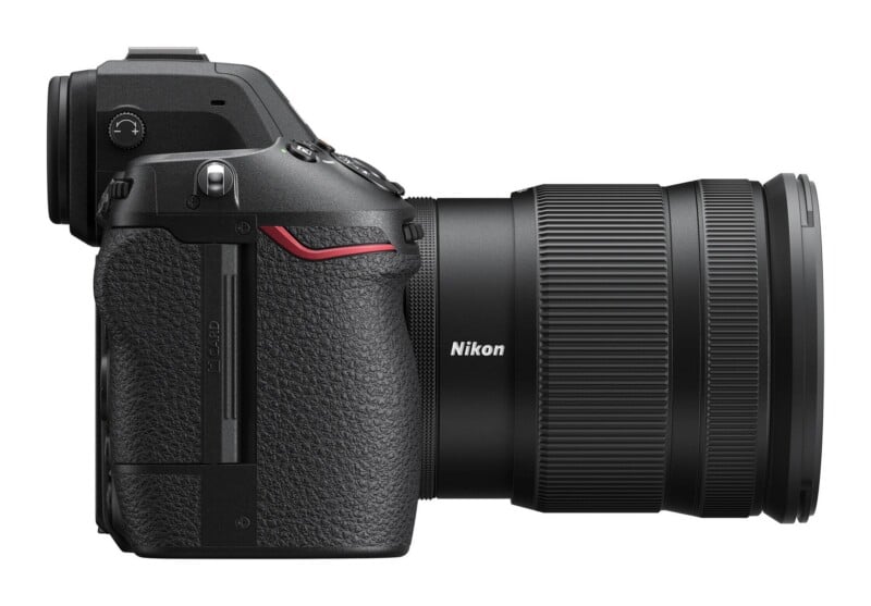 A side view of a black Nikon mirrorless camera with a lens attached, showing the textured grip, memory card slot door, and top control dials.