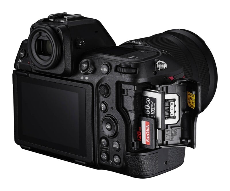 A black mirrorless camera shown from the rear, with its memory card slot door open to reveal a CFexpress card and a SanDisk SD card inserted.