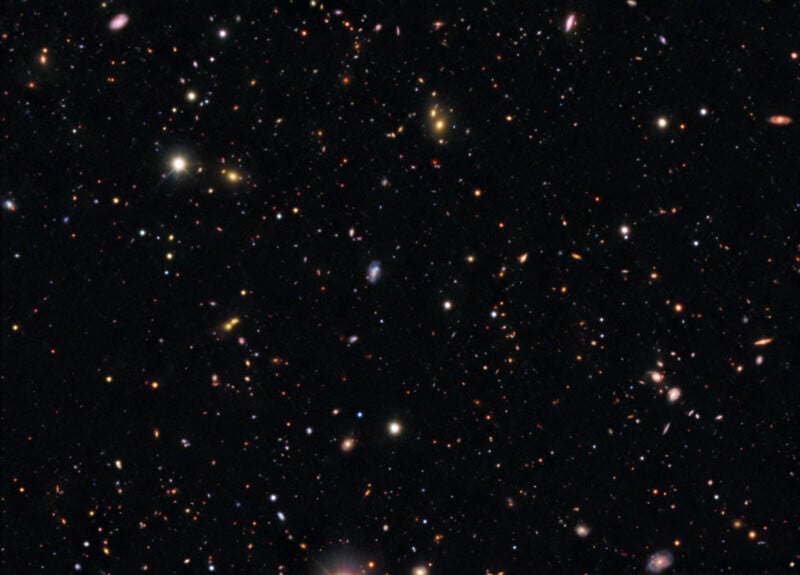 A deep-space view filled with thousands of distant galaxies of varying shapes, colors, and sizes against a black background.