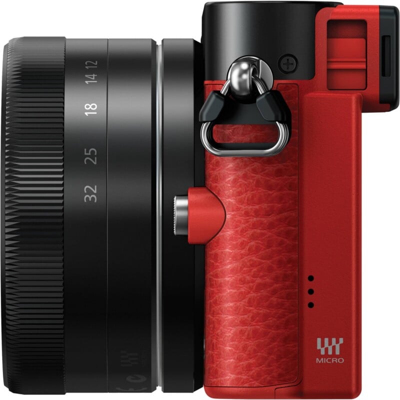 A side view of a red and black digital camera with a lens showing focal length markings from 12 to 32, featuring a textured red grip and a metal strap lug.
