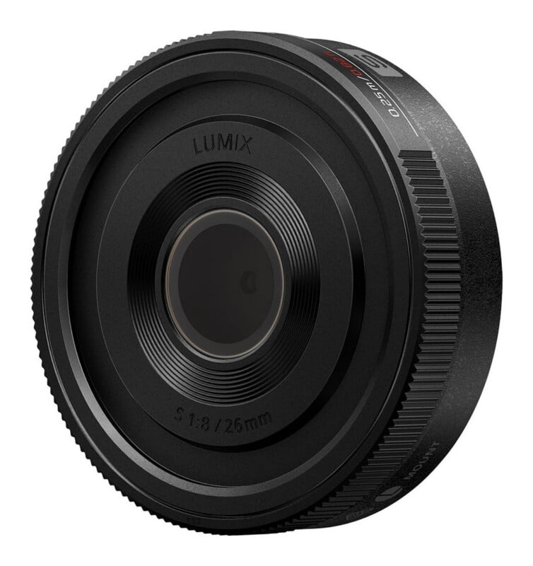 A black Lumix S 1:8 / 26mm pancake camera lens viewed from an angle, showing the front element and side focus ring.